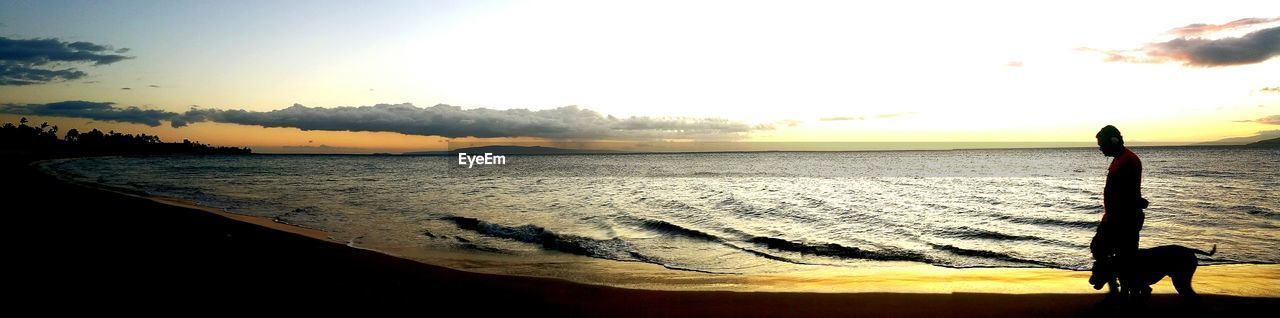 Panoramic view of man with dog at beach against sky during sunset