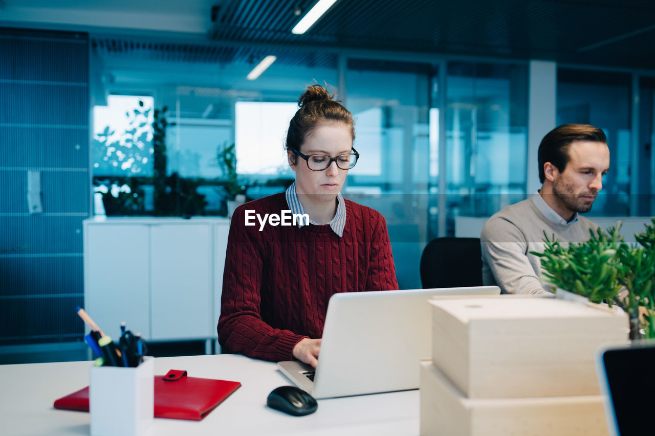 Businesswoman using laptop while sitting by colleague at desk in creative office