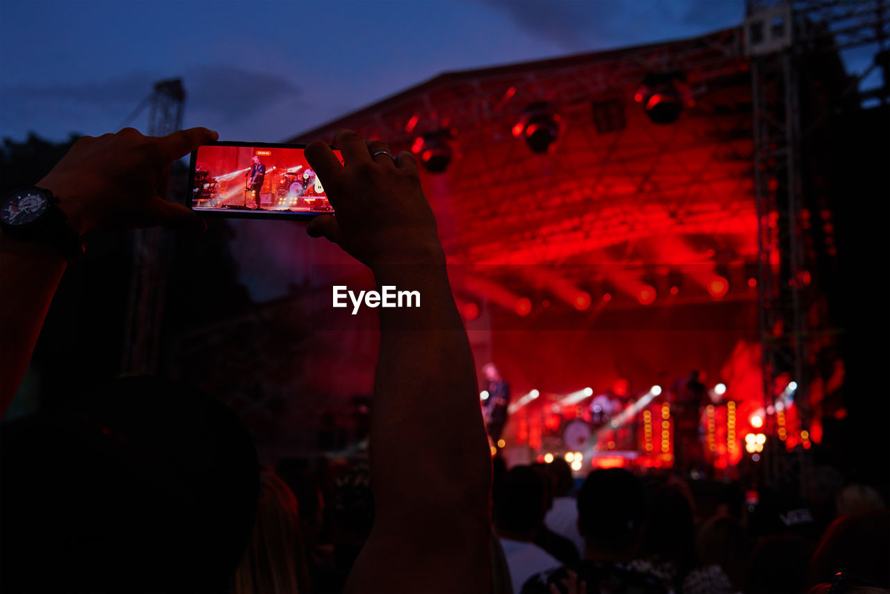 Person standing in front of stage, recording live music concert on smartphone