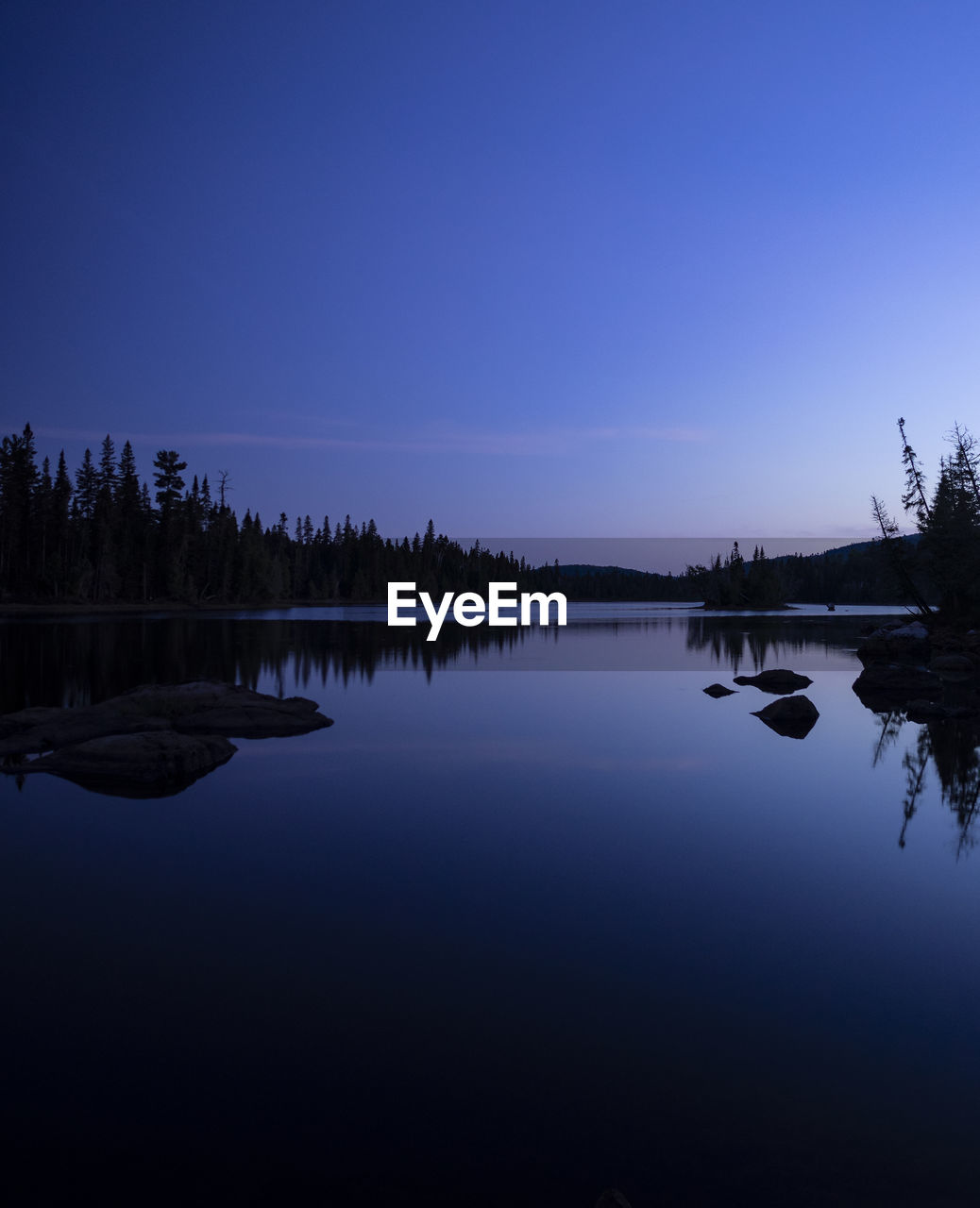 Scenic view of lake by trees against sky at dusk