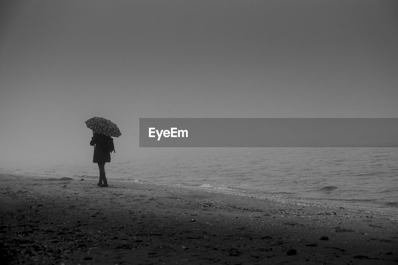 Rear view of woman standing on beach against sky