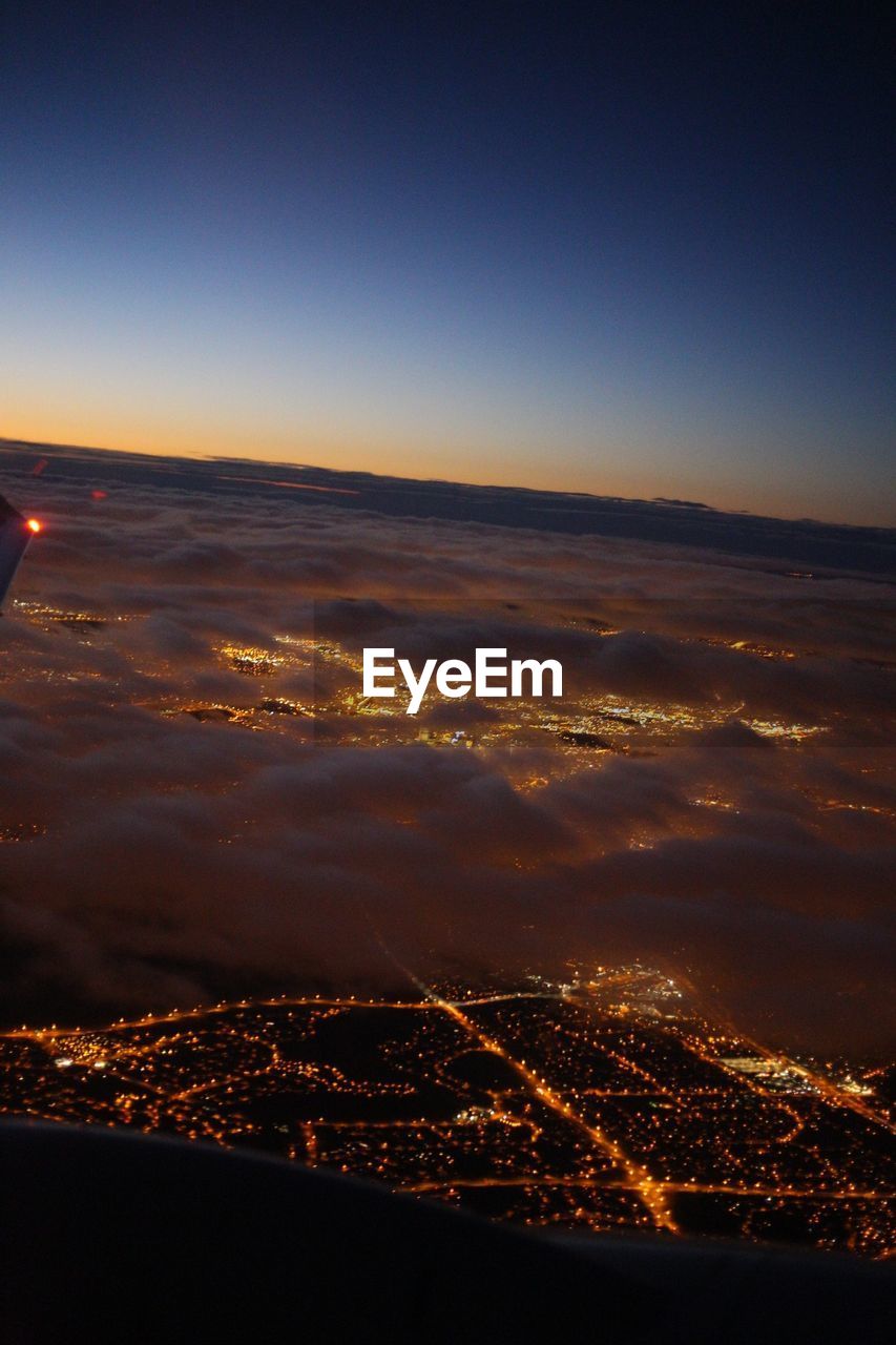 AERIAL VIEW OF ILLUMINATED CITYSCAPE AGAINST SKY AT NIGHT