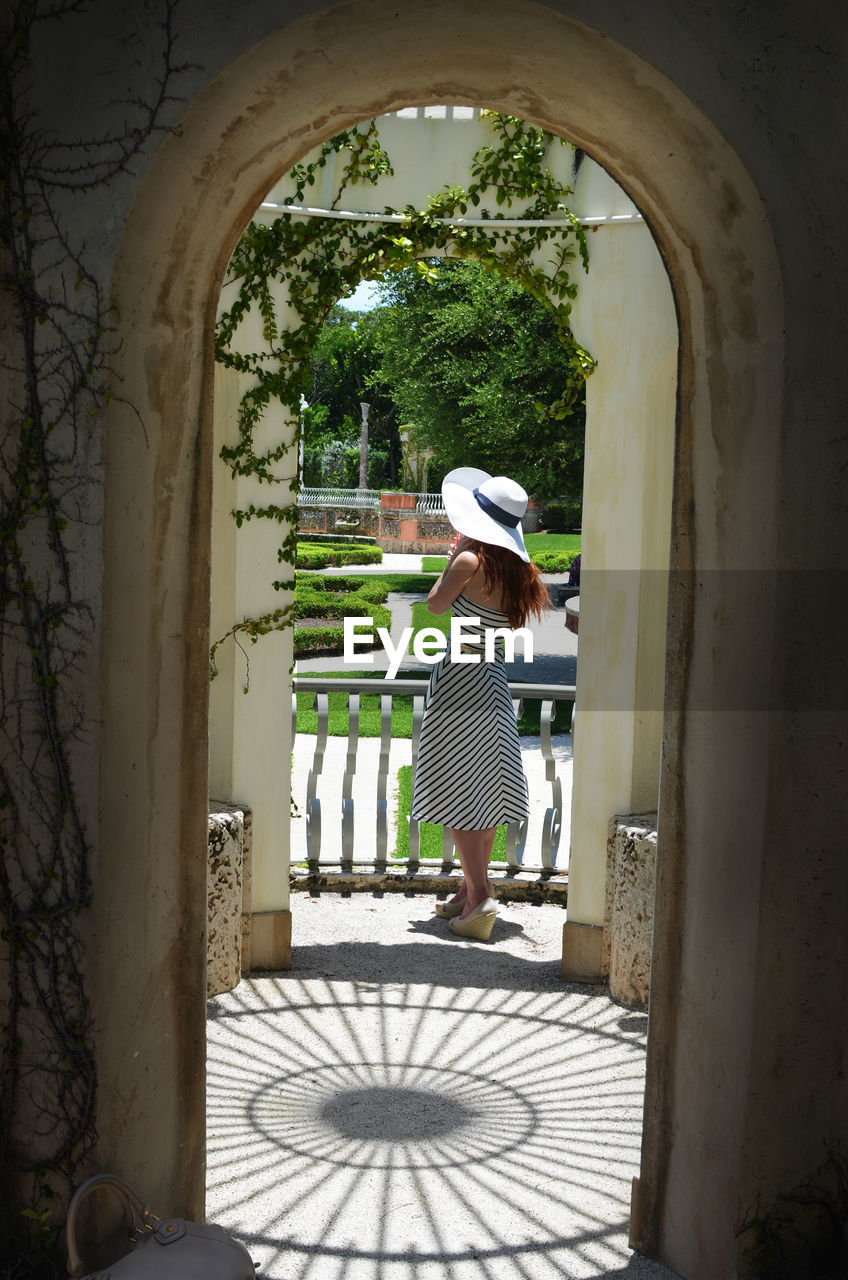 Full length of woman wearing hat seen through arch in park during sunny day