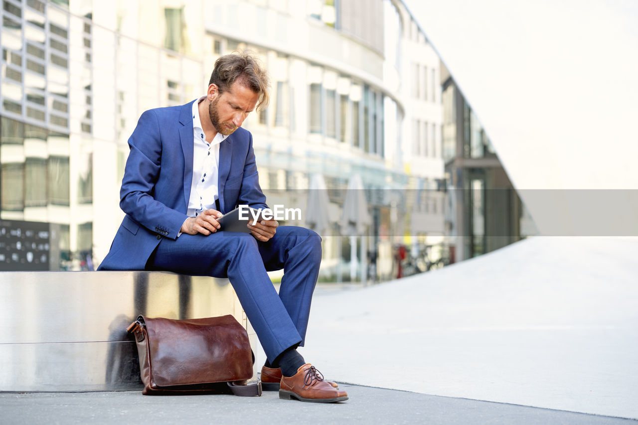 Businessman sitting on bench and using tablet pc in the city