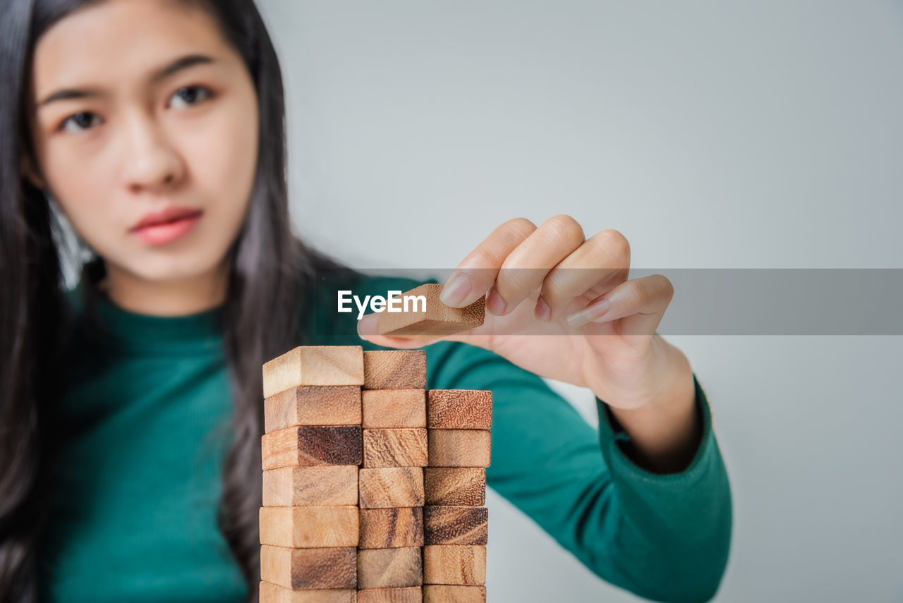 Close-up portrait of woman stacking toy blocks against white background