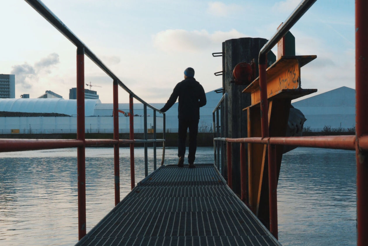 Rear view of man standing on metal pier over lake