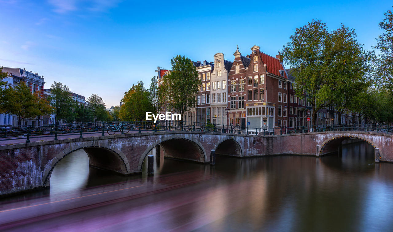 Arch bridge over river by buildings against sky