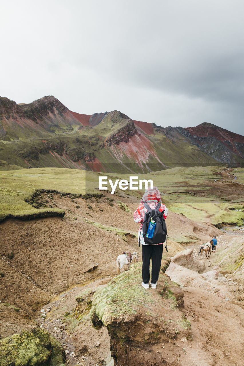 A young woman with a backpack is standing on a hill in peru