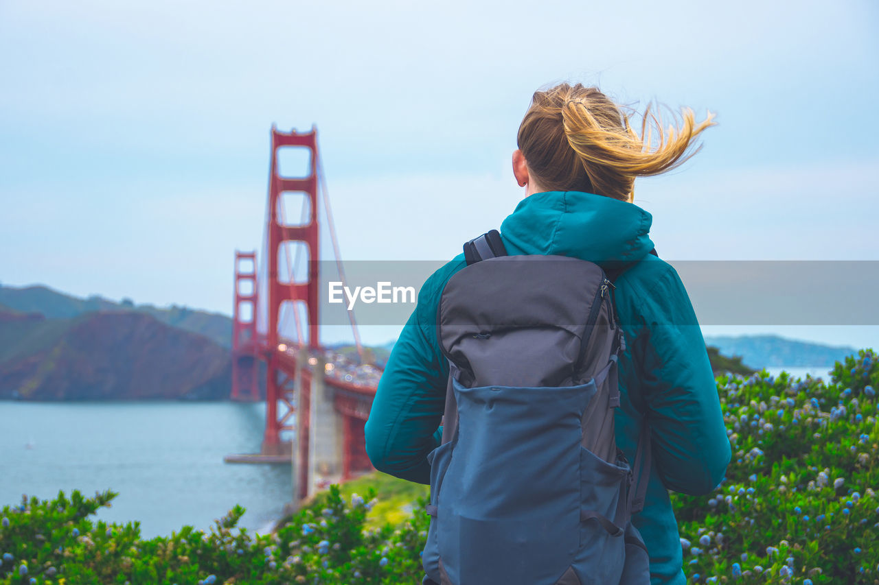 Rear view of backpack woman standing against golden gate bridge