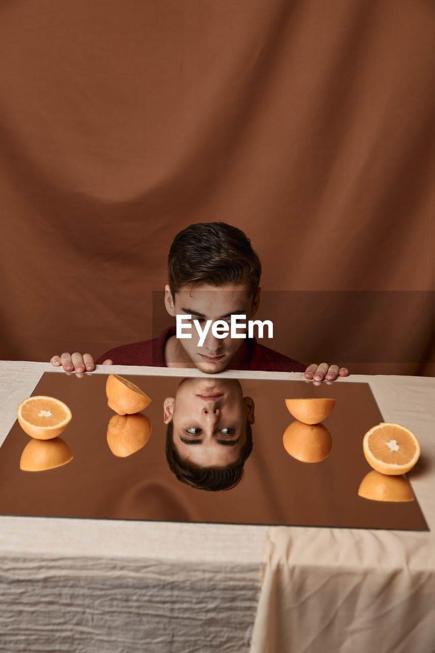 Man looking away with oranges on mirror against brown background