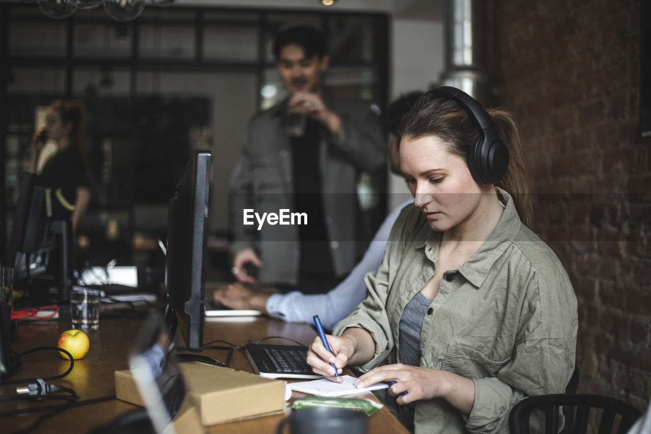 Businesswoman writing in note pad while working in office