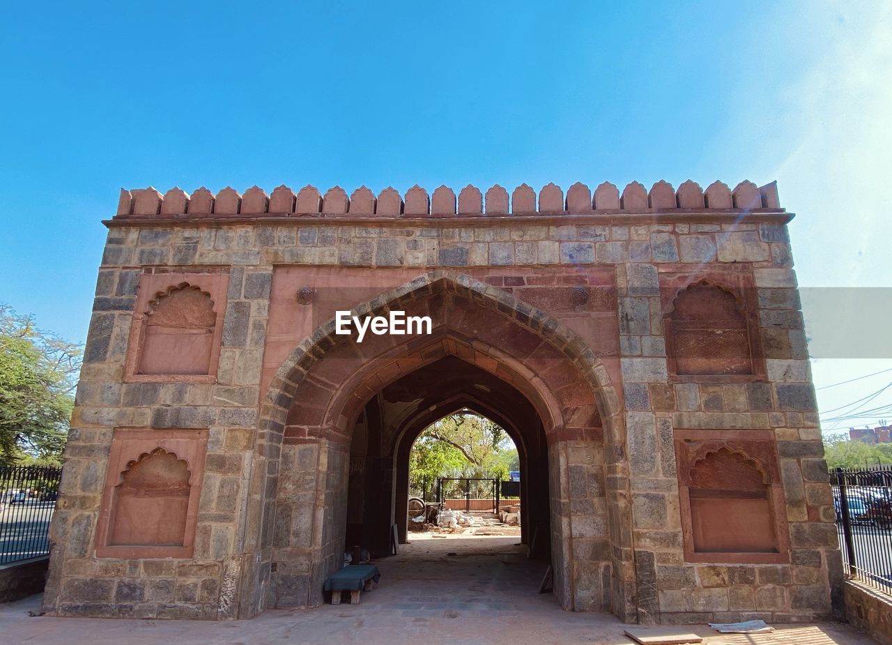 architecture, arch, landmark, history, built structure, the past, travel destinations, sky, nature, ancient history, gate, brick, city, travel, monument, triumphal arch, entrance, memorial, day, ancient, building exterior, blue, no people, outdoors, historic site, street, tourism, clear sky, calligraphy, plant