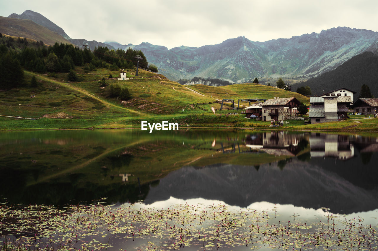 SCENIC VIEW OF LAKE BY HOUSES AGAINST MOUNTAINS