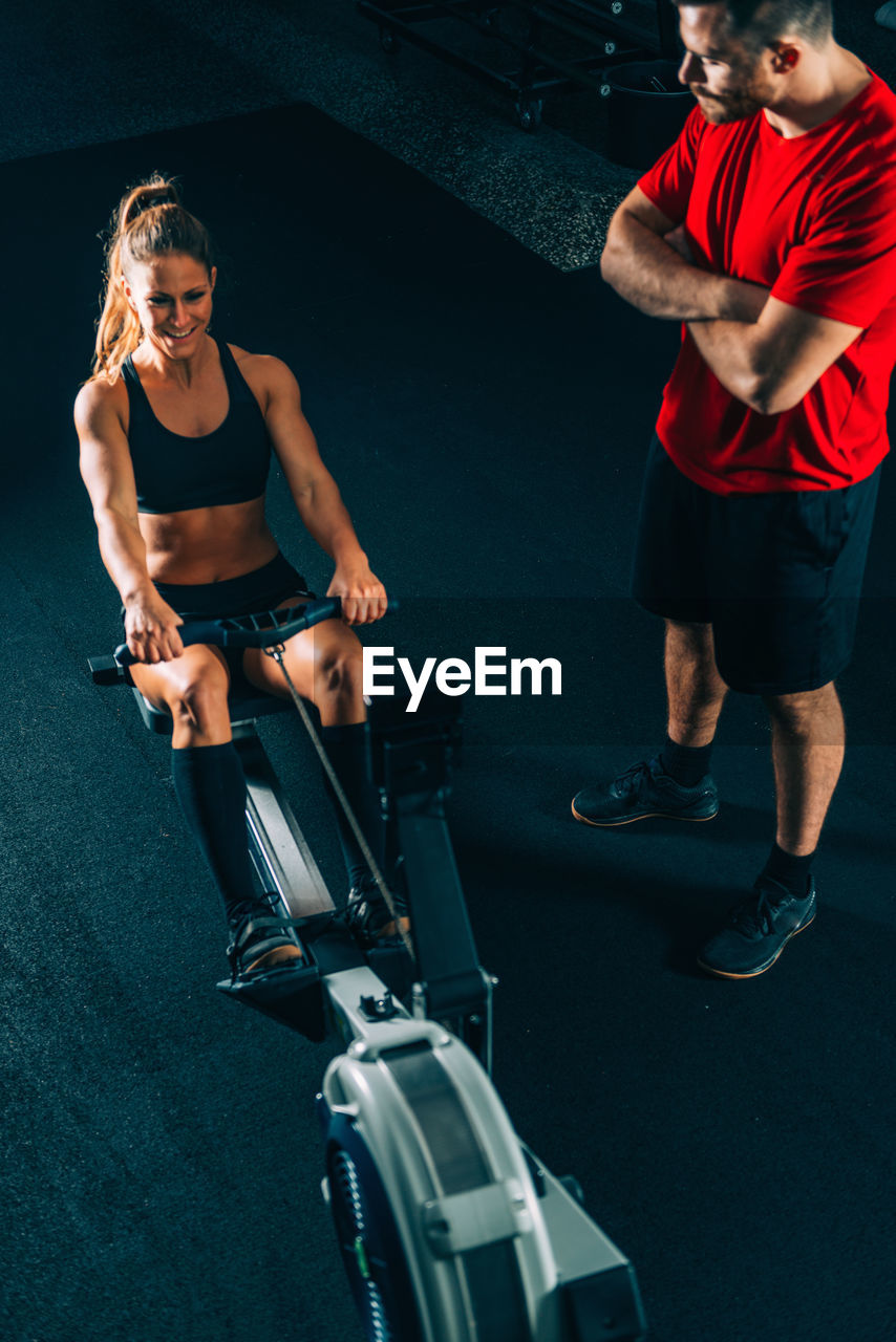 High angle view of coach standing by woman exercising at gym