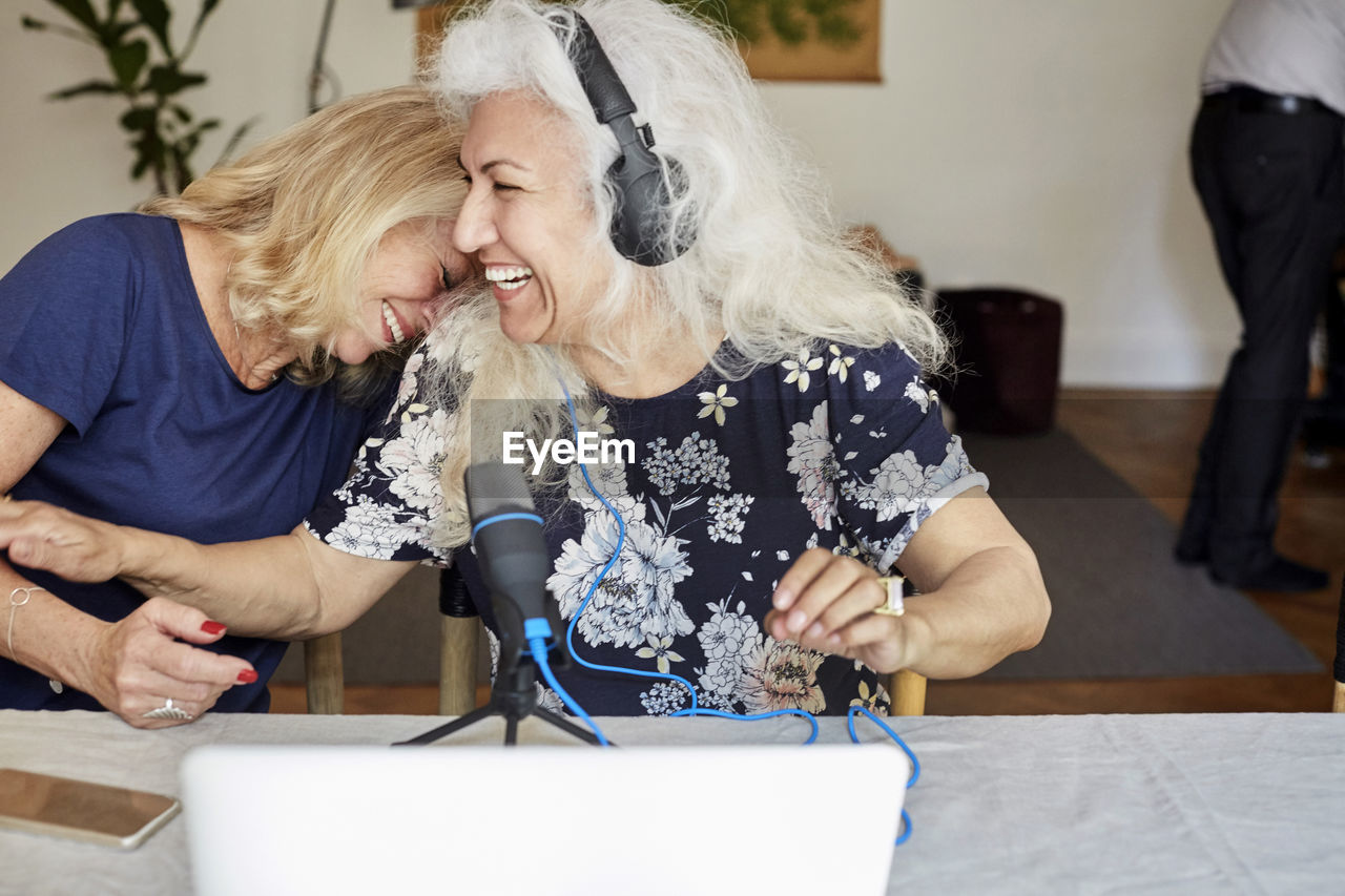Cheerful senior friends vlogging through laptop at home