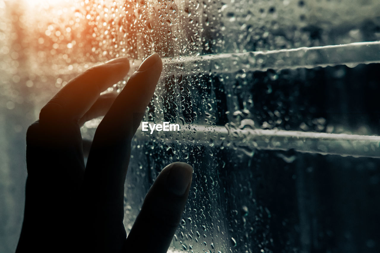 Close-up of hand on wet window during rainy season