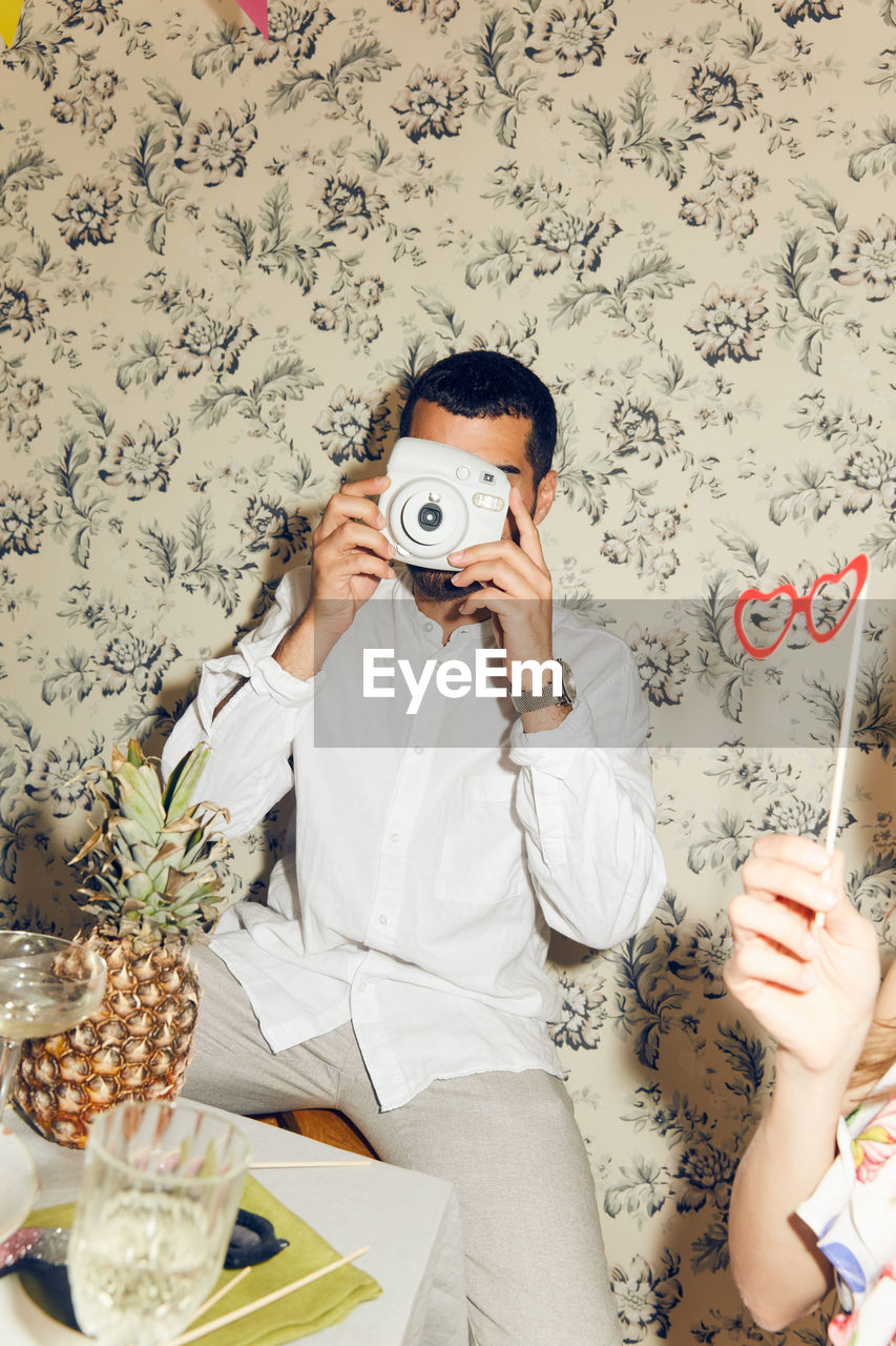 Young man photographing while sitting during dinner party at home