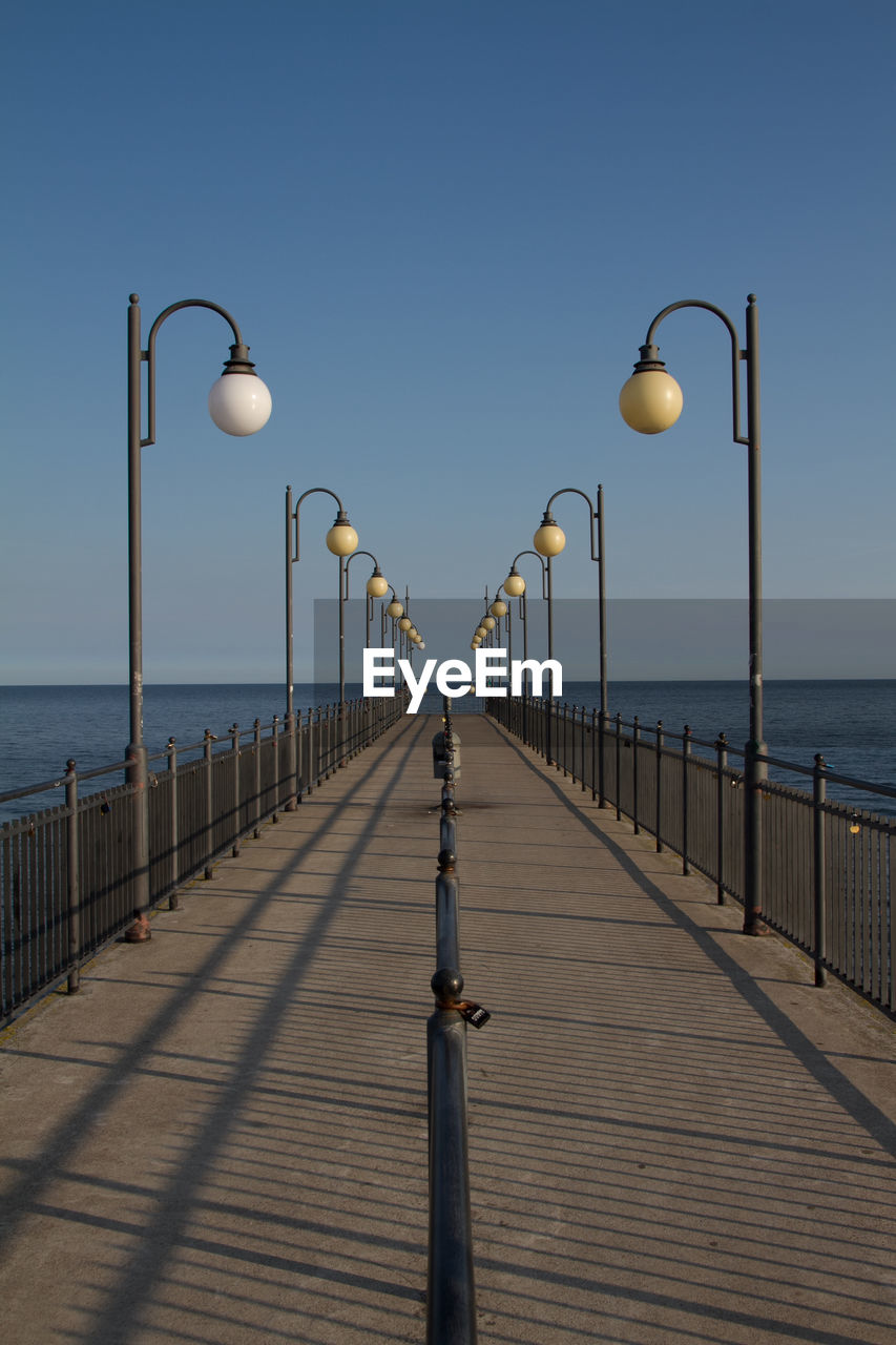 Street lights on pier by sea against clear sky