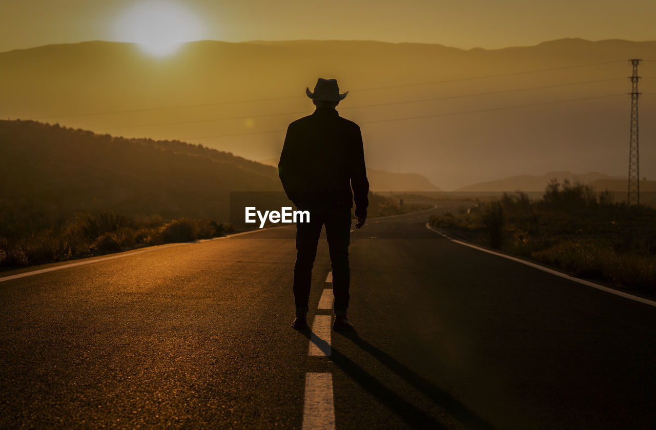 Silhouette of adult man in cowboy hat standing on country road during sunset. almeria, spain