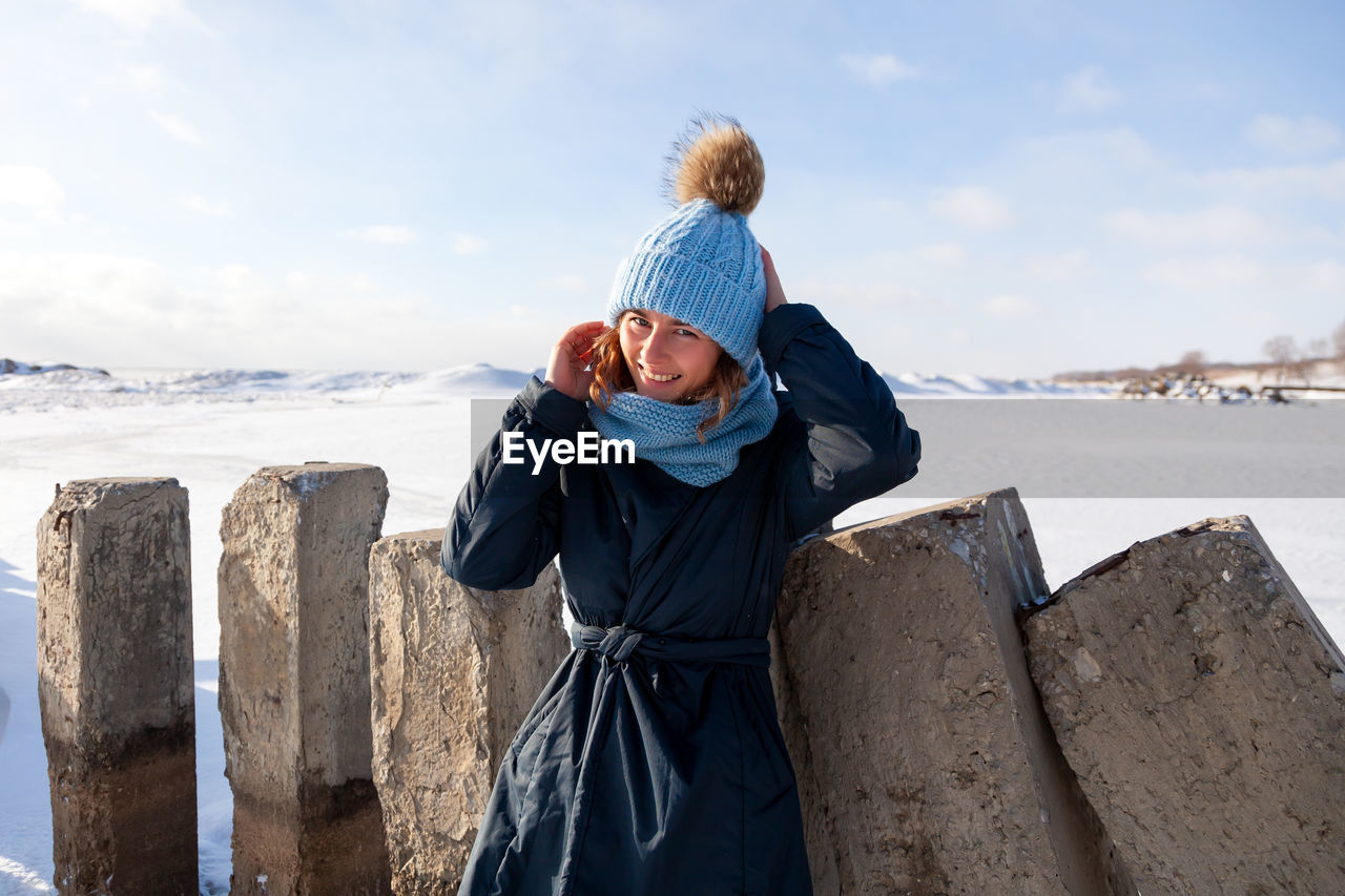 A young woman in a blue knitting hat, black coat enjoys winter nature, walking on the frozen sea 