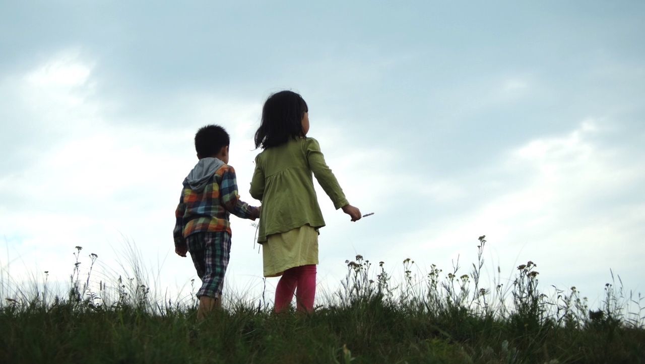 Rear view of children holding hands against sky