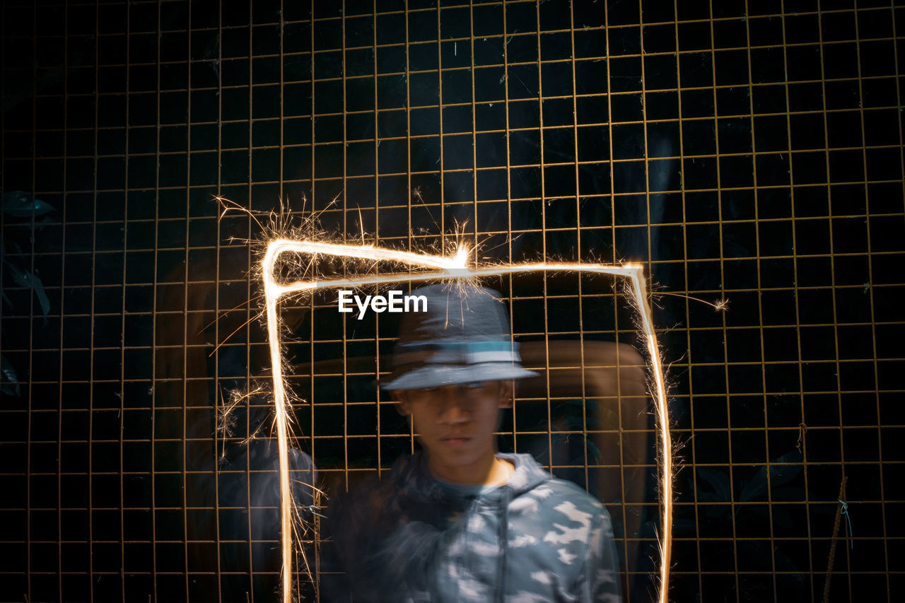 Man standing amidst light painting against fence