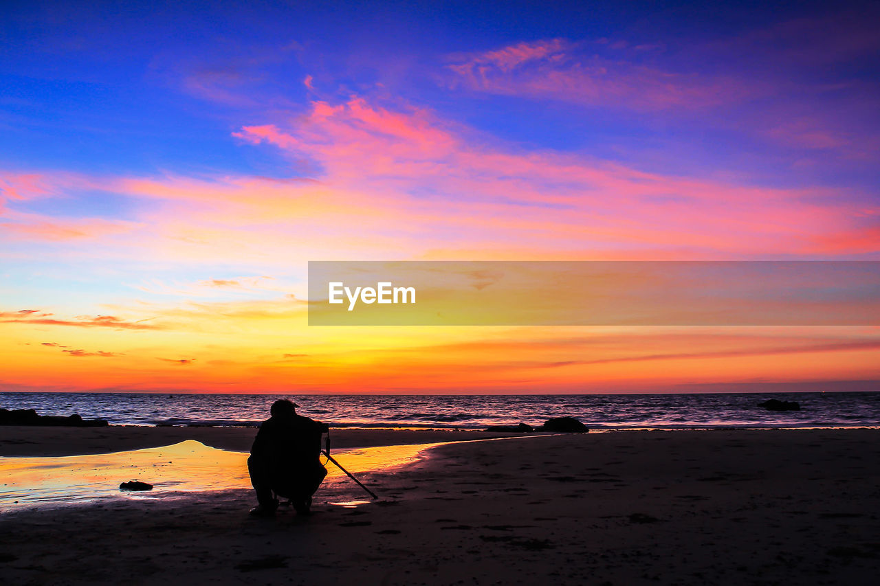 SILHOUETTE MAN ON BEACH AGAINST ORANGE SKY