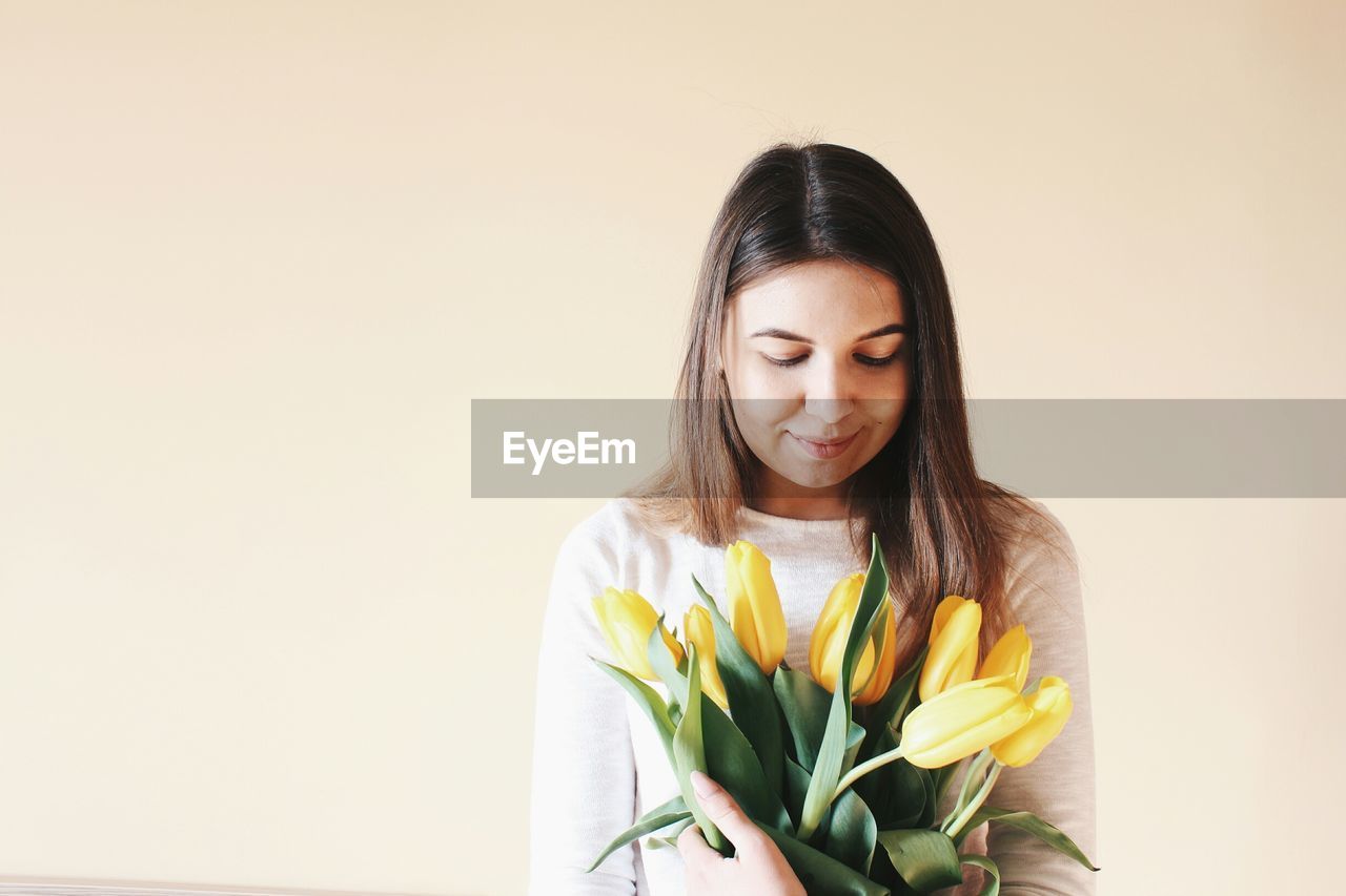 Close-up of young woman with yellow flowers against colored background