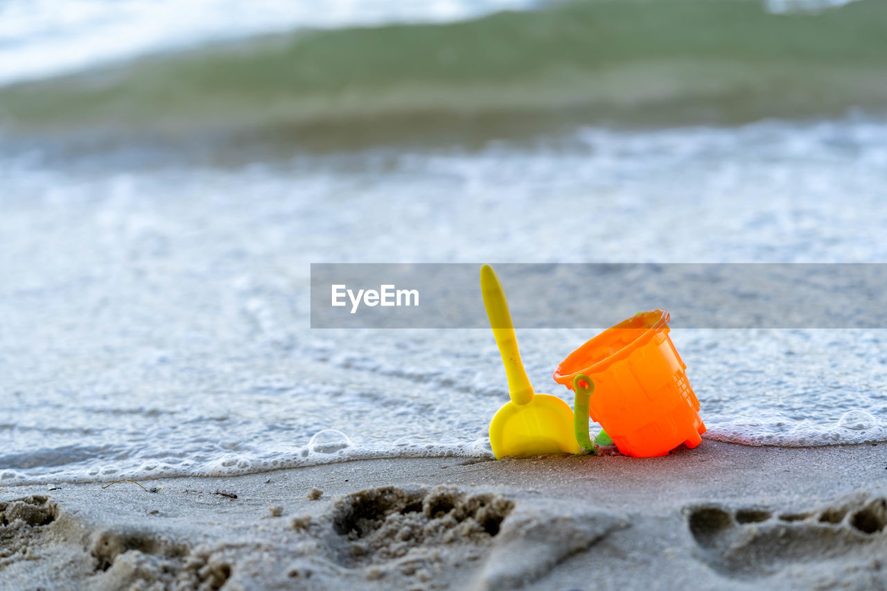 CLOSE-UP OF YELLOW TOY ON SANDY BEACH