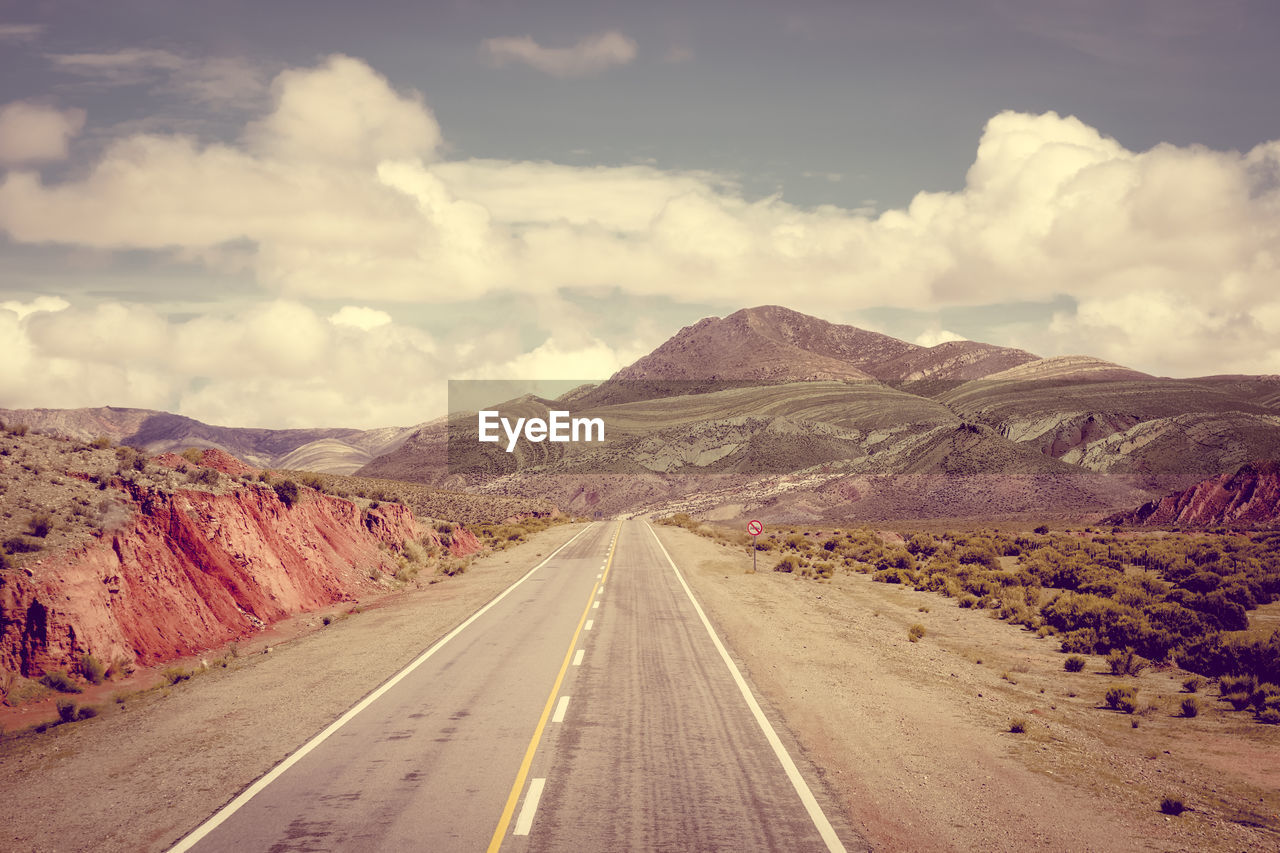 EMPTY ROAD ALONG LANDSCAPE WITH MOUNTAINS IN BACKGROUND