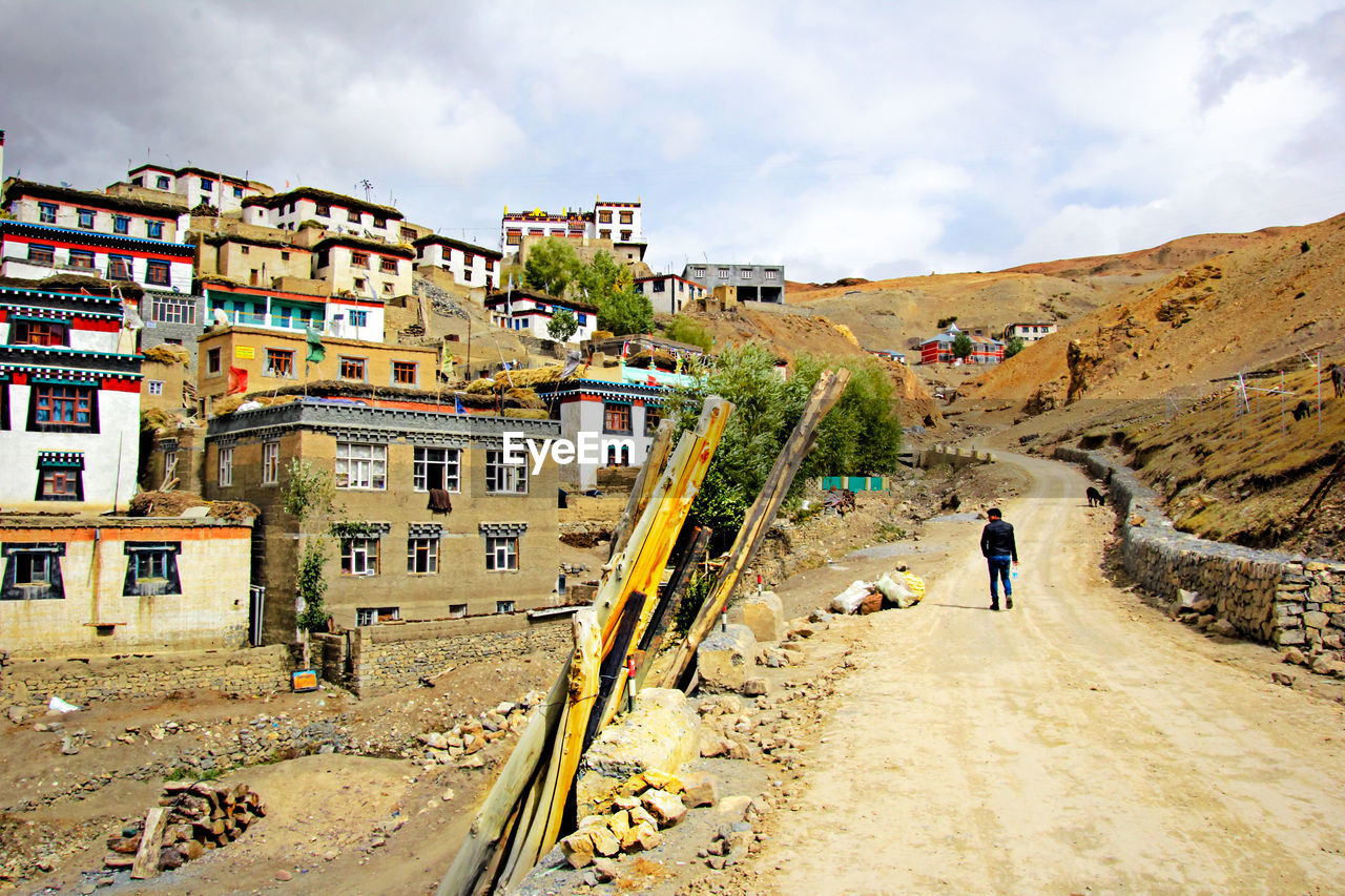 PEOPLE WALKING ON ROAD AMIDST BUILDINGS AGAINST SKY