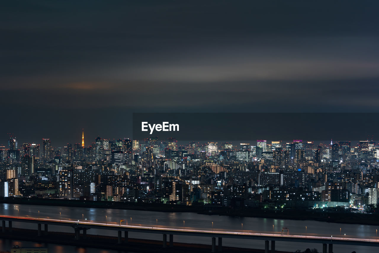 Illuminated cityscape by river against sky at night