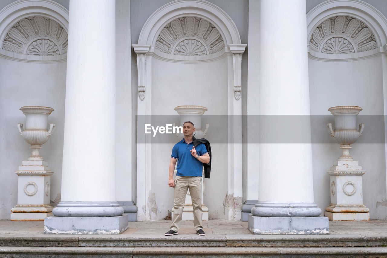 A man in casual clothes stands near the columns of a white building person