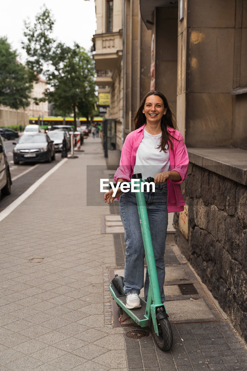 Young woman in pink shirt ride electric kick scooter on city street. alternative, ecology transport.