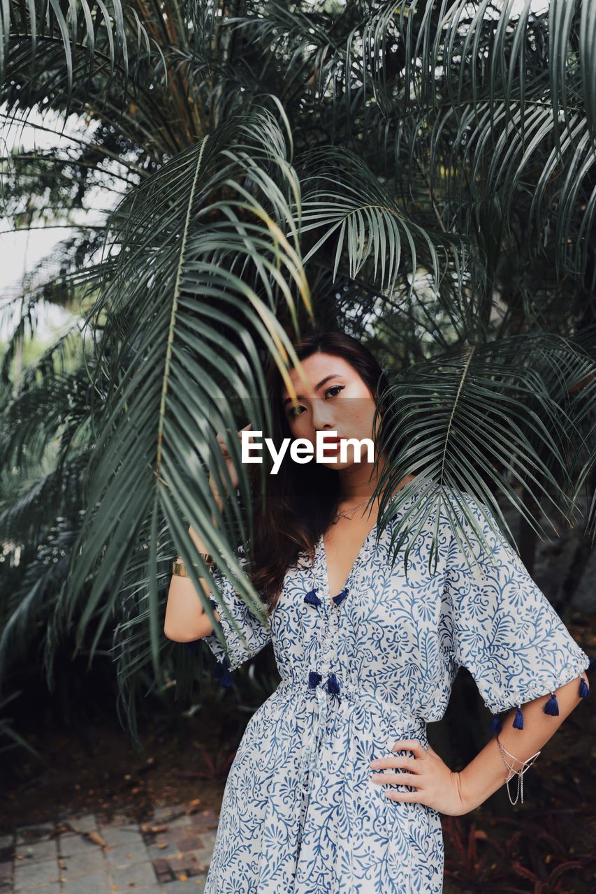 YOUNG WOMAN STANDING WITH PALM TREE