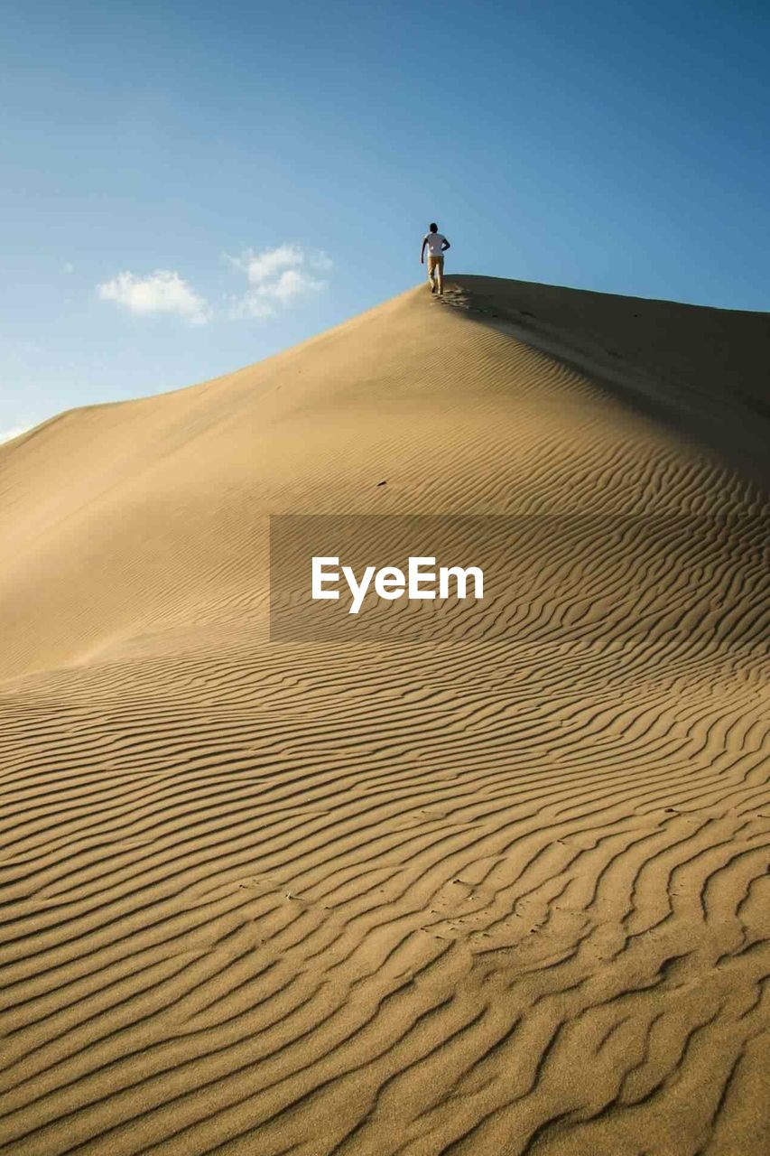 Man walking on sand dune in desert against sky