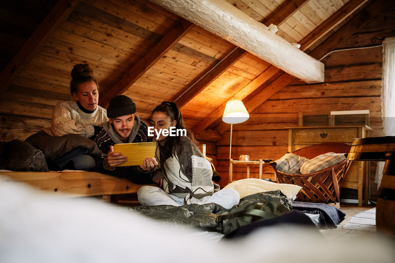 Male and female friends watching movie over digital tablet while relaxing in cottage