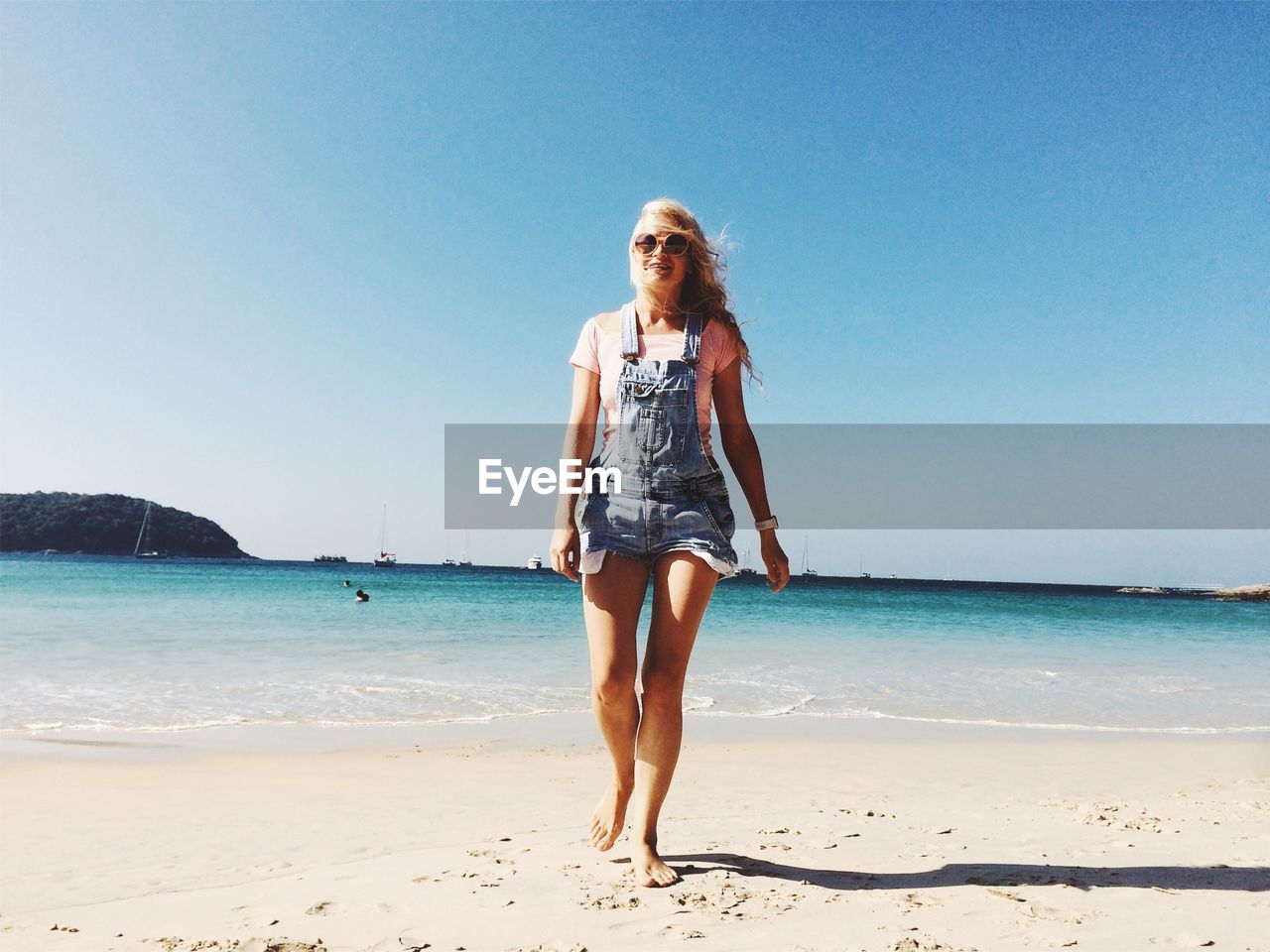 Full length of young woman walking at beach against clear sky