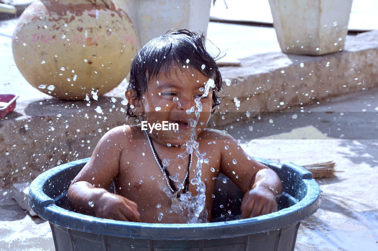 Shirtless baby boy splashing water in bucket