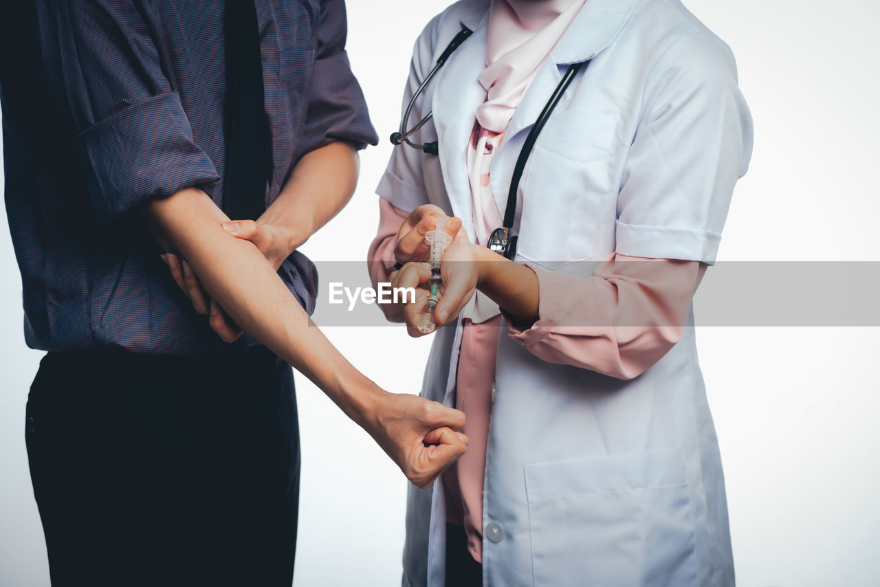 Midsection of man holding hands before a doctor giving a shot. 