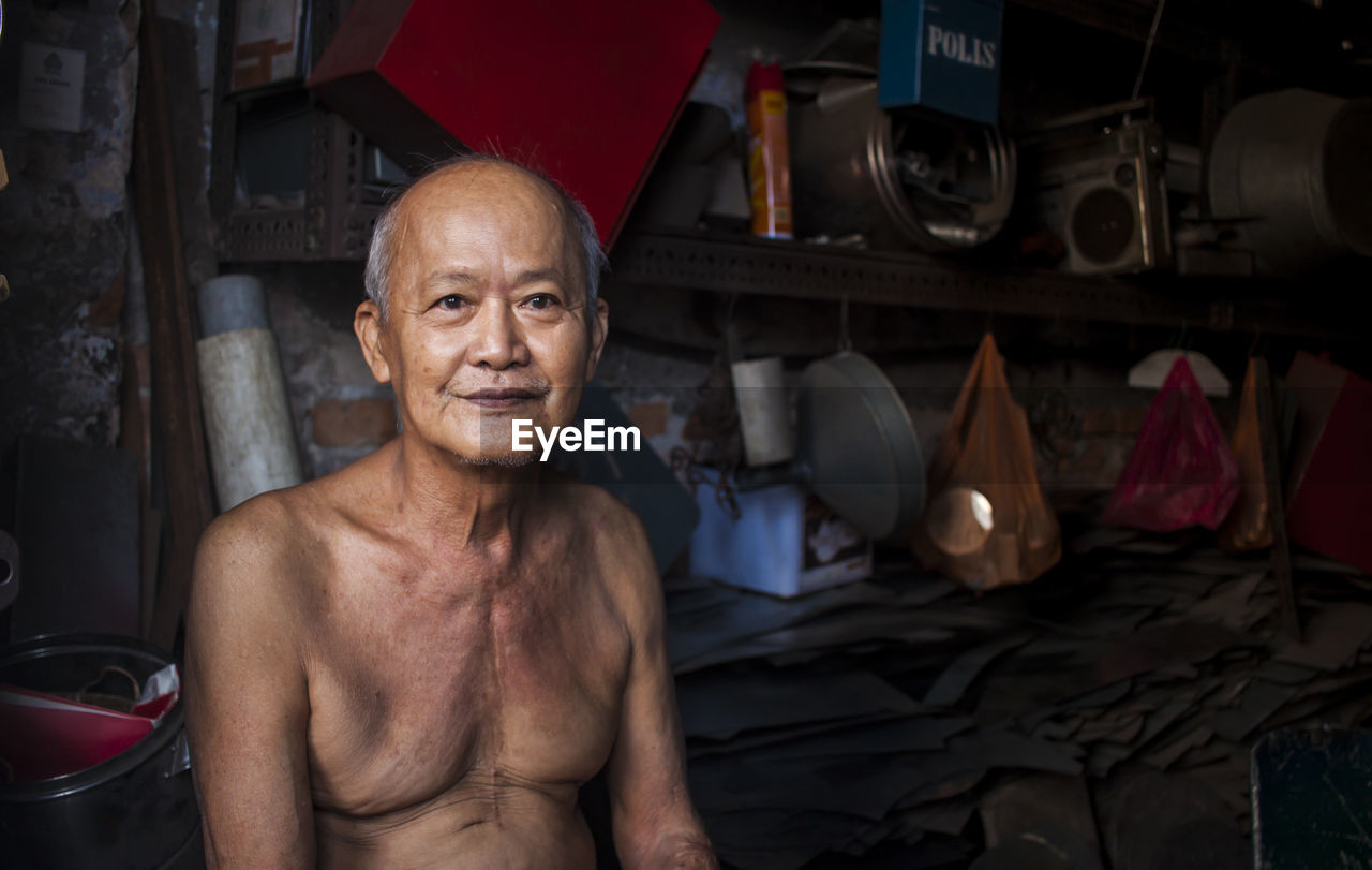 Portrait of smiling shirtless mature man sitting in warehouse