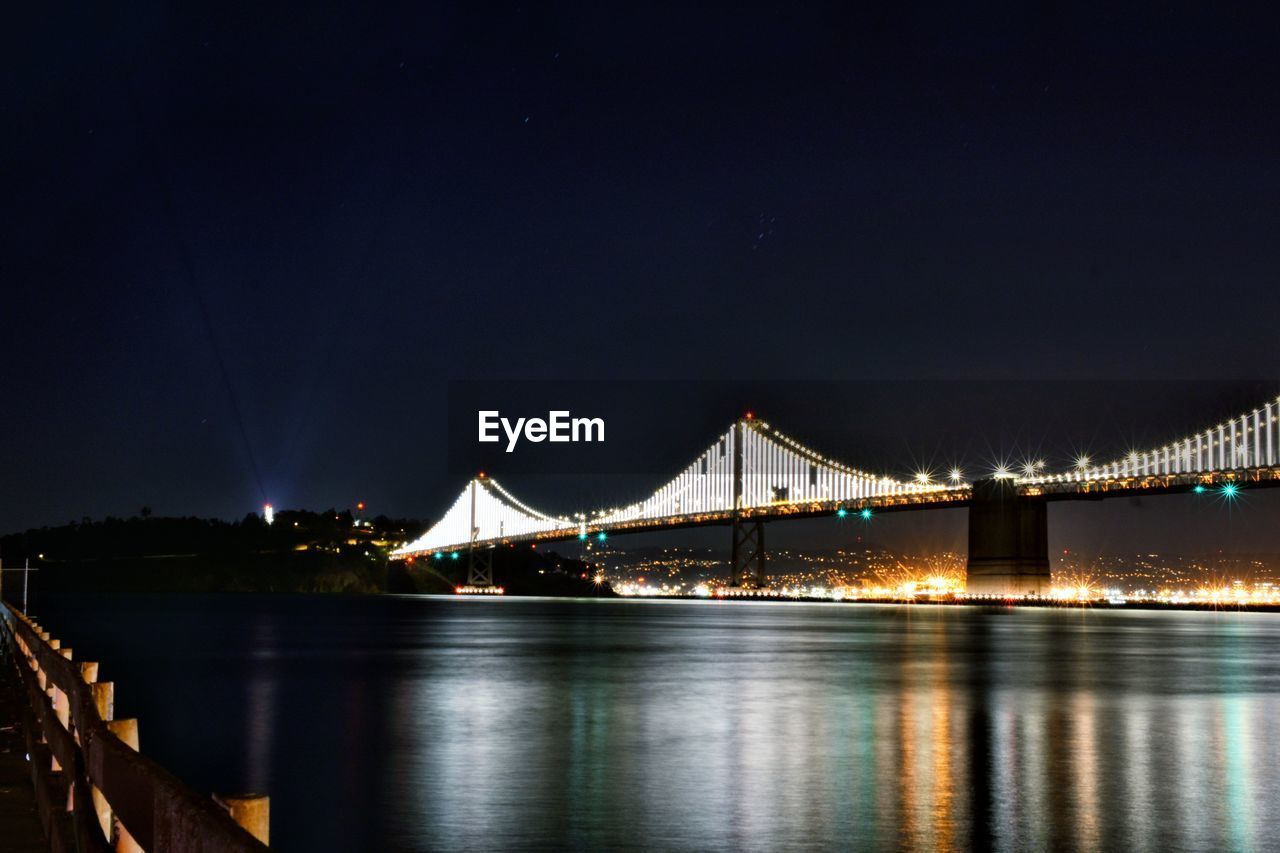 Illuminated bridge over calm river at night