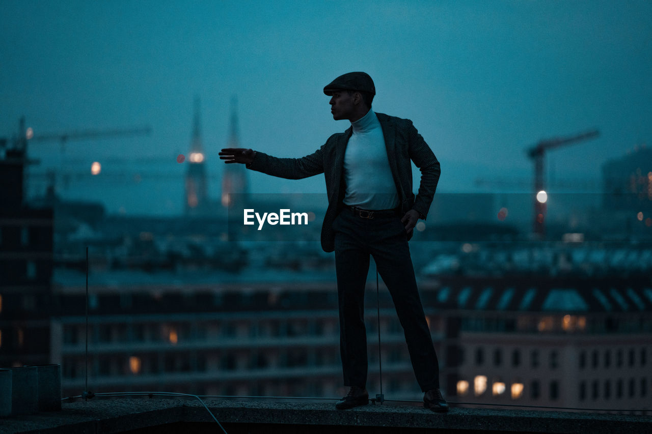 FULL LENGTH OF MAN STANDING AGAINST CITYSCAPE AT DUSK