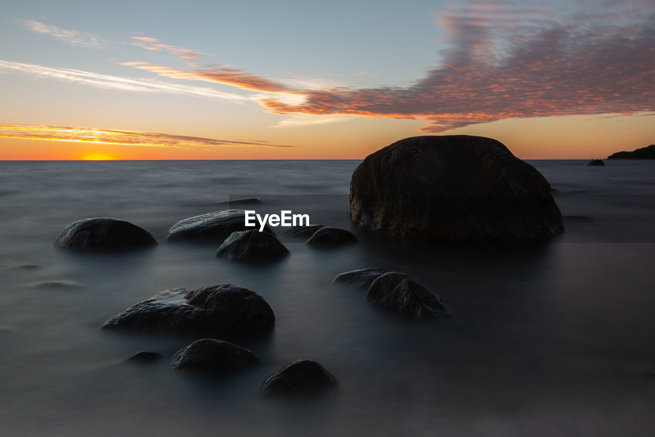 Rocks on beach against sky during sunset