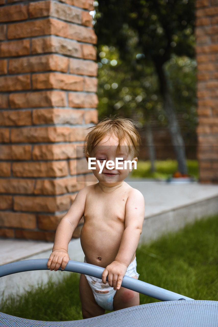 Little boy laughing in the yard of a house on the street in diapers