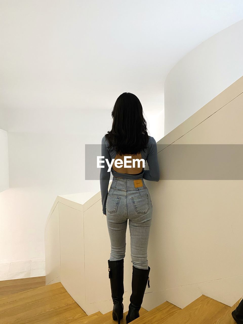 REAR VIEW OF WOMAN STANDING ON WALL AT HOME