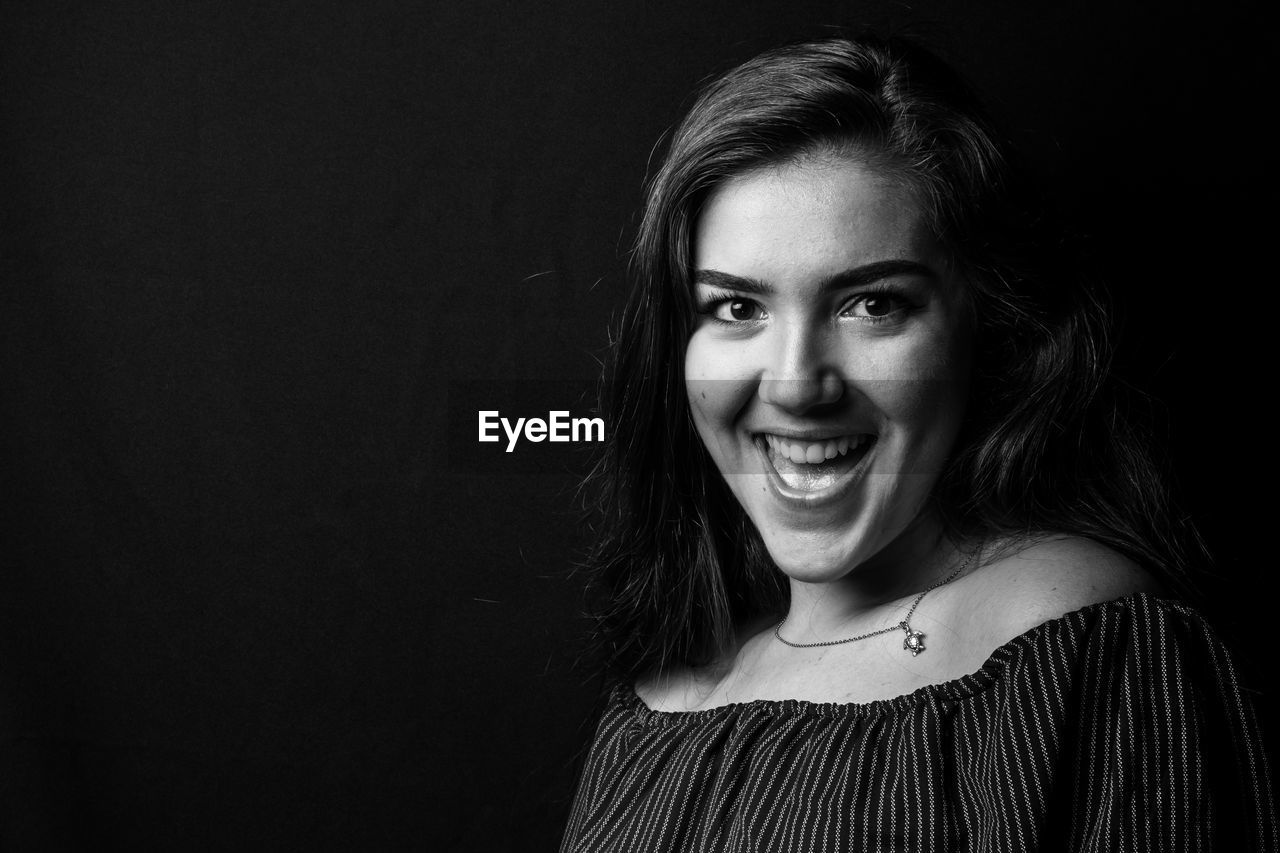 Portrait of smiling young woman against black background