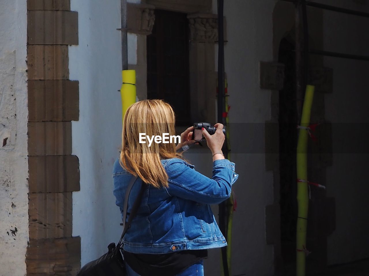 Woman photographing while standing against building