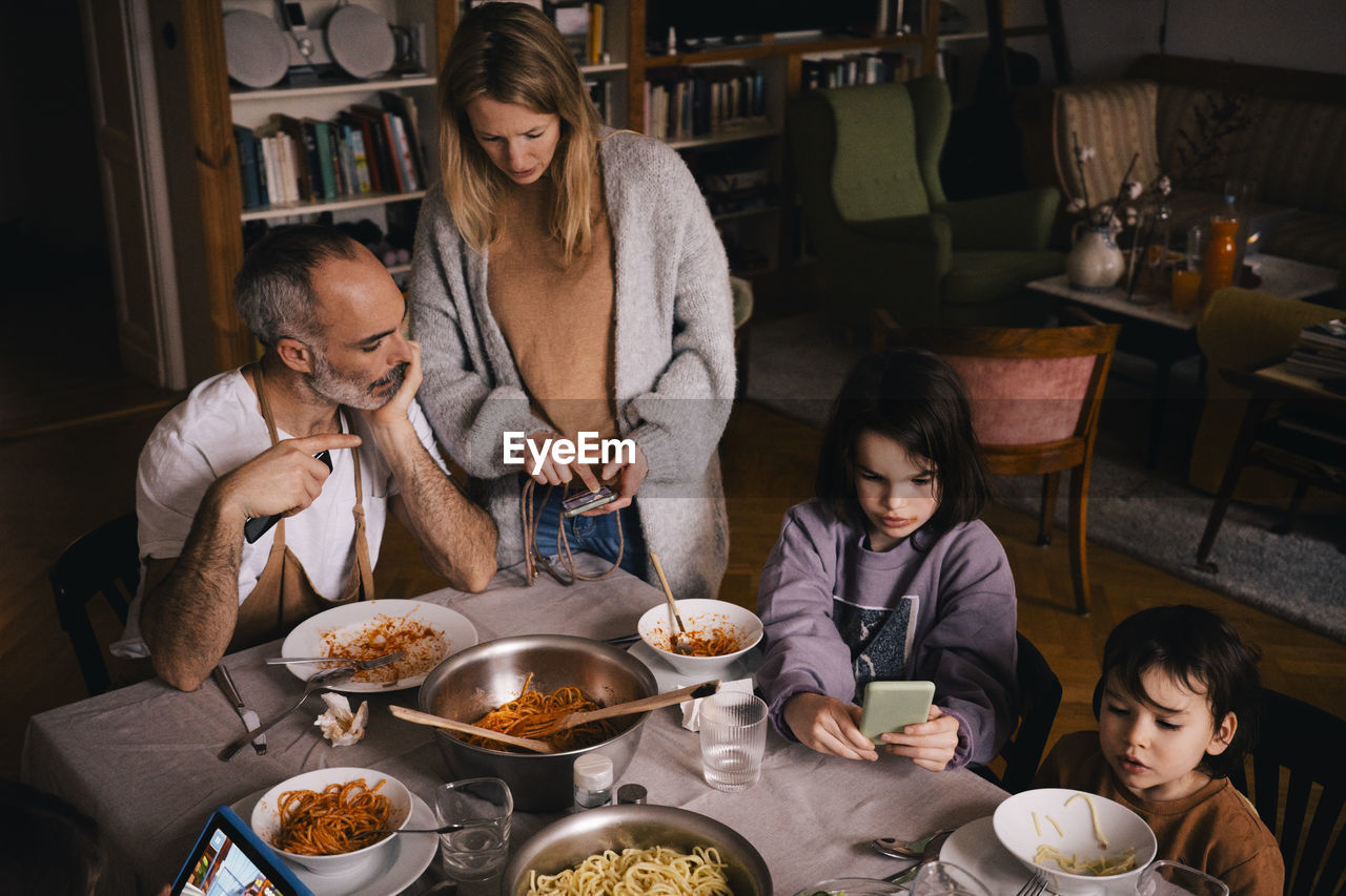 Family with spaghetti using smart phones at dining table