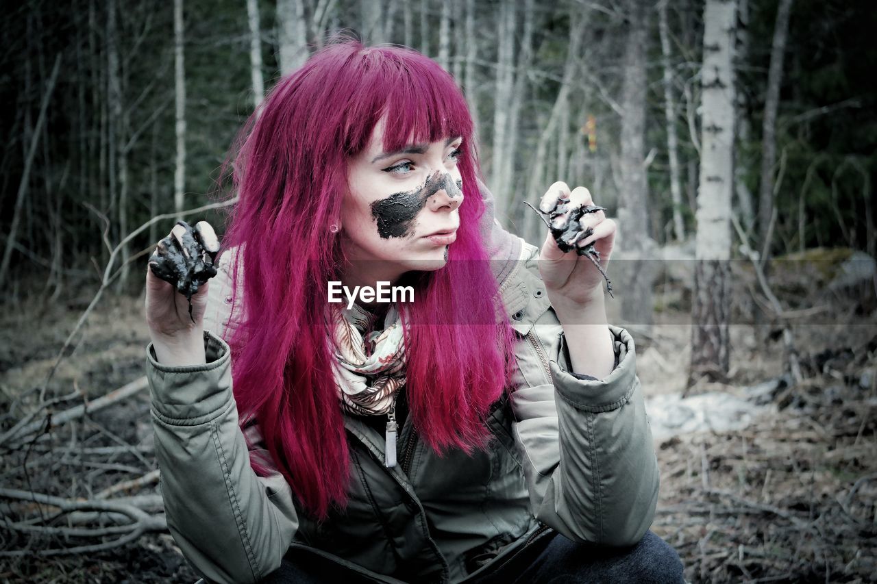 Redhead woman with mud on face crouching in forest